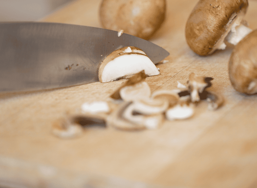white mushrooms being sliced on cutting board