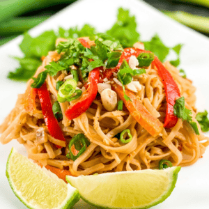 vegetarian pad thai with 2 lemon wedges on a white plate