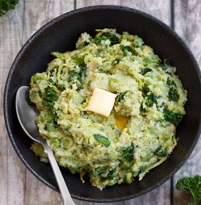 vegan colcannon in a cast iron skillet with a serving spoon and pat of butter on top