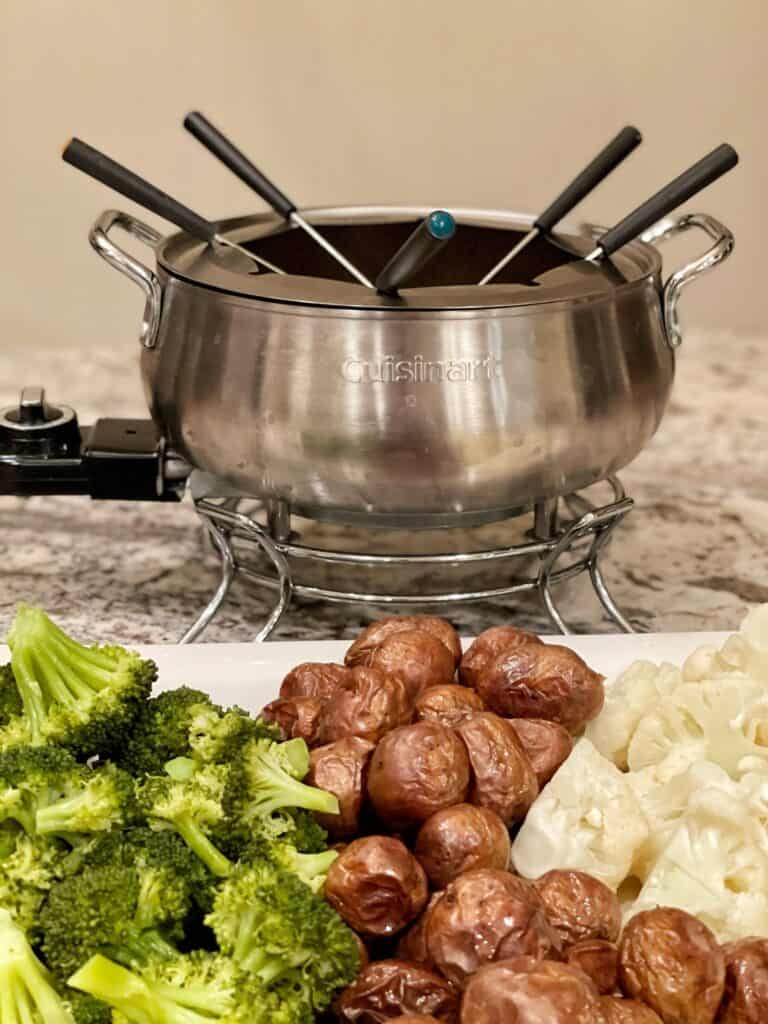 fondue with cauliflower, potatoes and broccoli cut into bite sized pieces beside fondue bowl