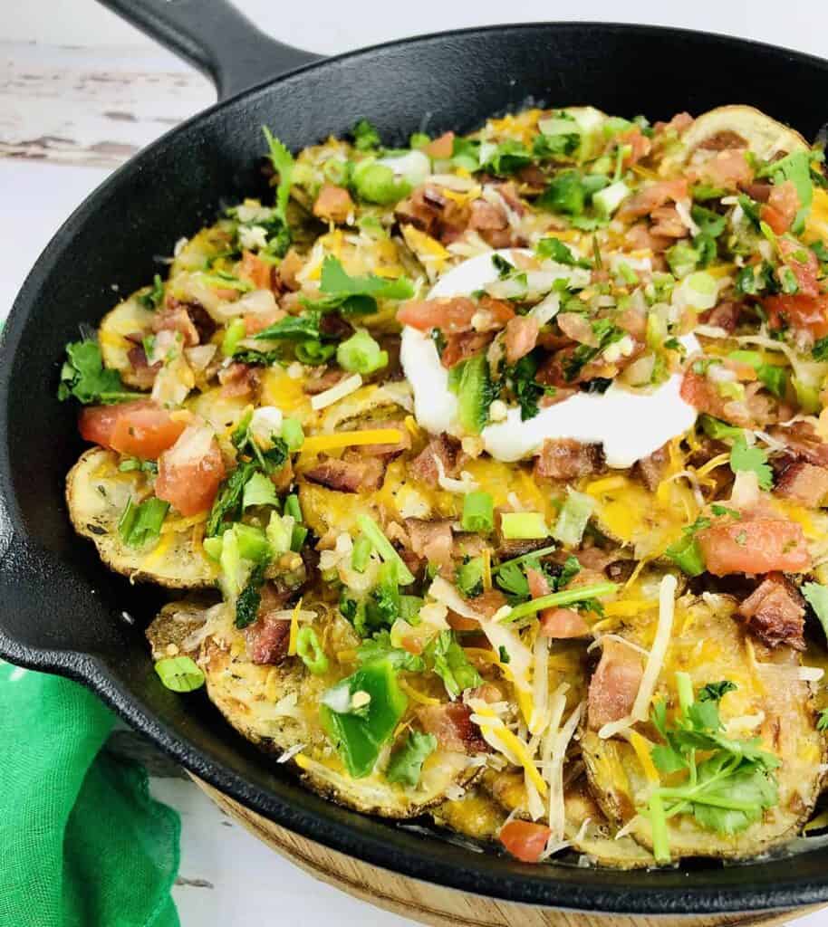 cast iron skillet with potato nachos and toppings of cheese, tomatoes, corned beef, green onions