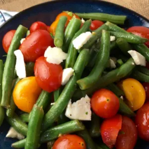 green bean salad with cherry tomatoes and cheese in dark bowl