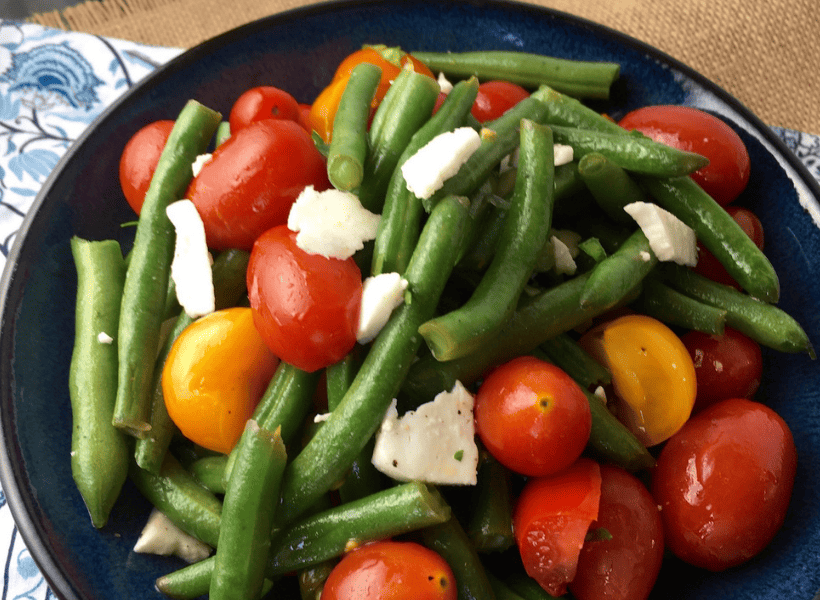 green bean salad with cherry tomatoes and cheese in dark bowl