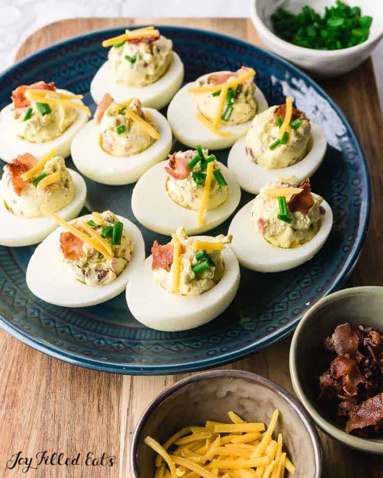 keto deviled eggs with bacon on cutting board with side dishes of cheese and bacon