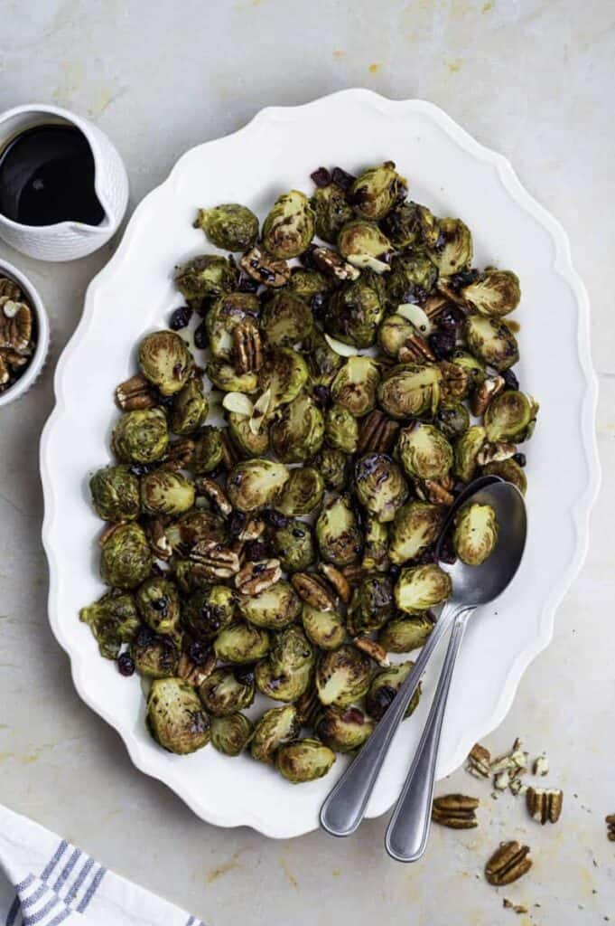 roasted brussels sprouts with balsamic glaze on white serving platter with spoons