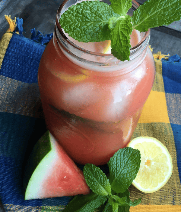 mason jar with mint garnishment and watermelon lemonade with lemon and watermelon beside it