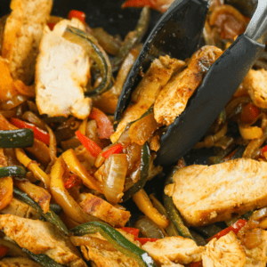 chicken fajitas cooked in cast iron skillet with tongs picking some up