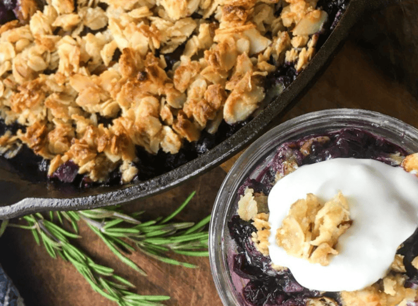 blueberry crisp in cast iron pan with serving of crisp with yogurt topping in glass dish