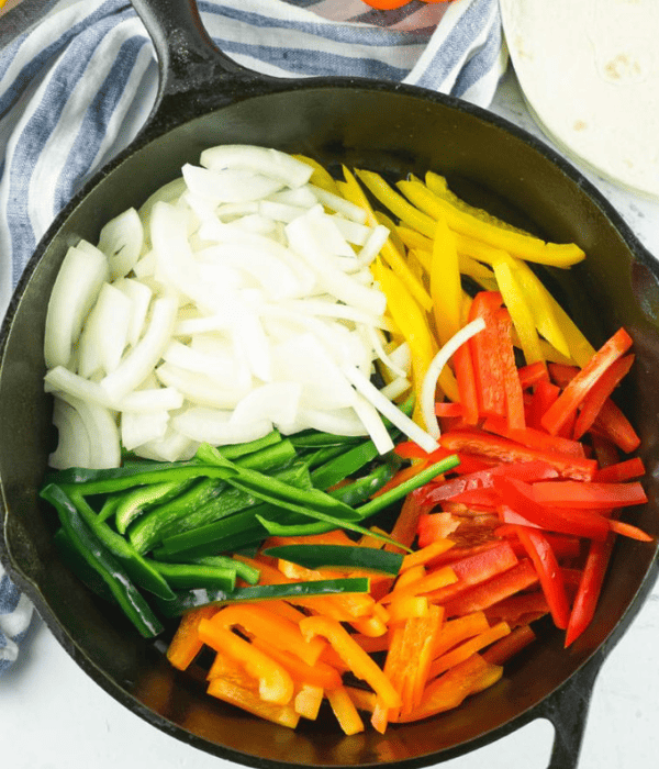 cast iron skillet with sliced peppers, sliced onions ready to cook