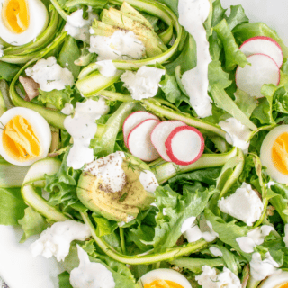 shaved asparagus with lettuce, hard boiled eggs, avocado and dressing on a white plate