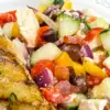 pan seared mahi mahi on plate with tomato cucumber kalamata olives salad