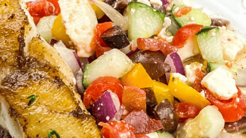pan seared mahi mahi on plate with tomato cucumber kalamata olives salad