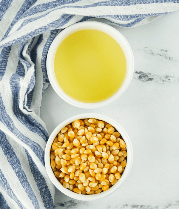 oil and popcorn kernels in small bowls with towel beside on counter