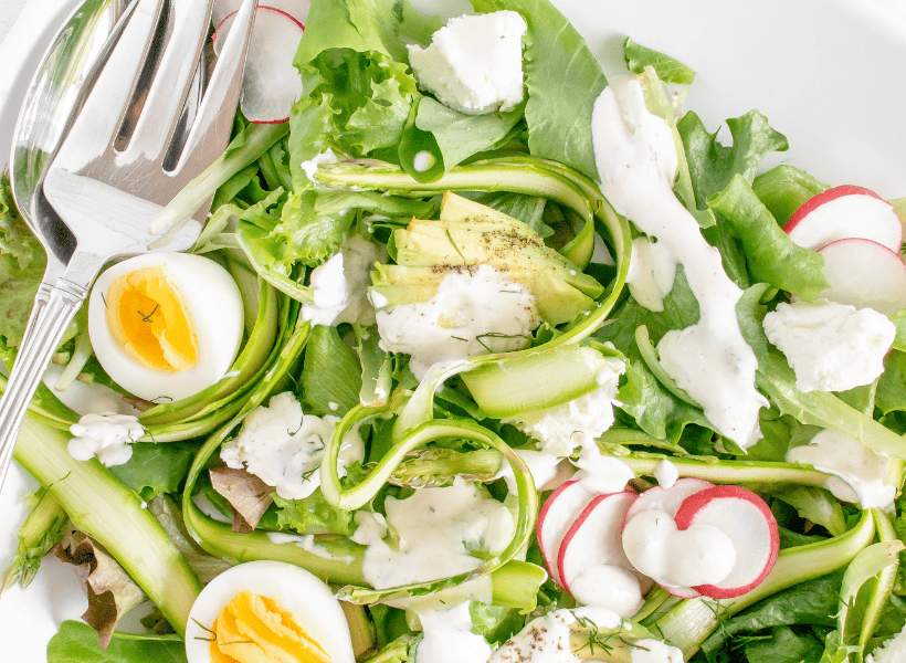 asparagus salad with hard boiled eggs, raddishes, lettuce and dressing on plate with fork