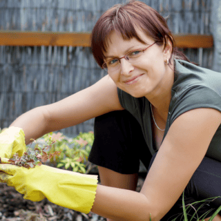 woman working in garden with yellow gloves looking at camera