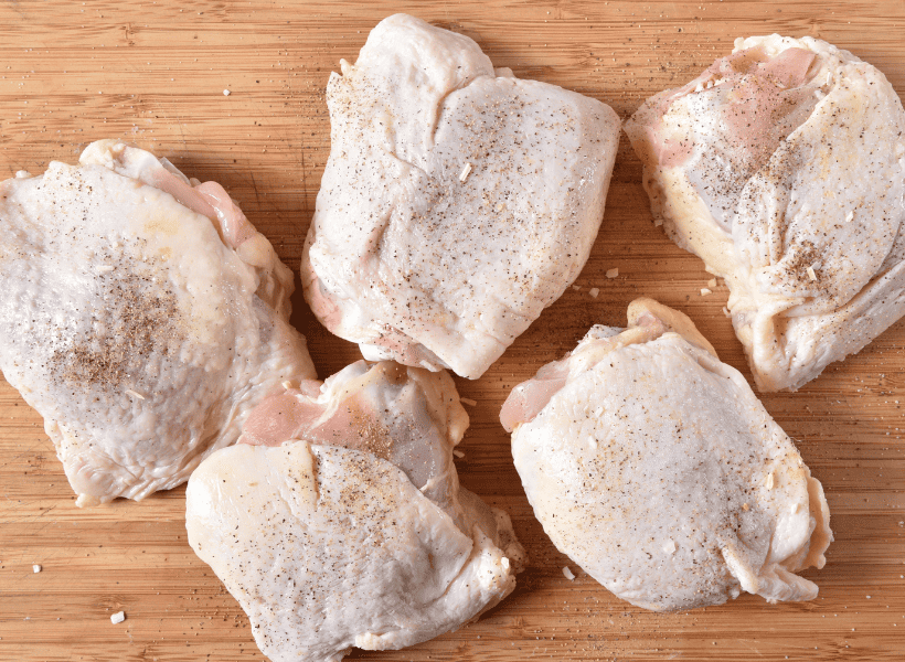 raw chicken thighs seasoned with pepper on cutting board