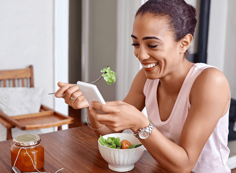 woman eating salad at table looking at phone