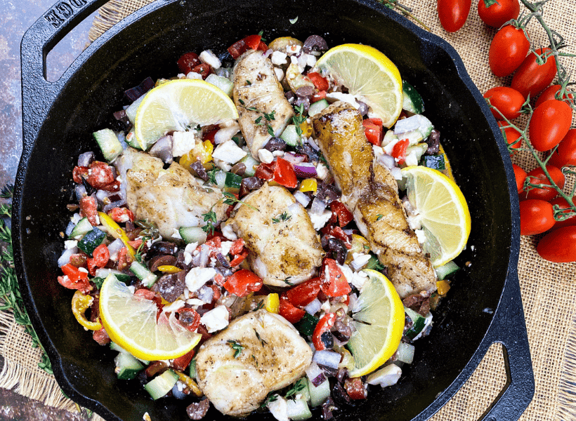 mahi mahi cooked with olives, tomatoes, lemon, beans and onions in a cast iron skillet 
