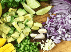 chopped avocado, red onion, garlic, jalapeno, mango and lime for salsa on cutting board