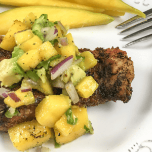 red snapper with cajun seasoning and mango salsa on a white plate with a fork