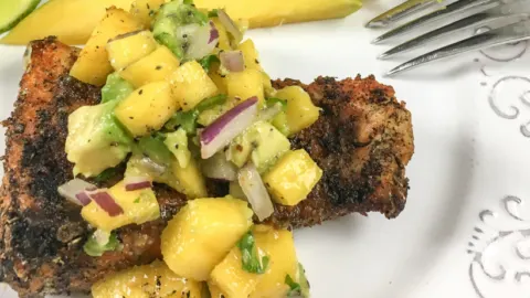 red snapper with cajun seasoning and mango salsa on a white plate with a fork