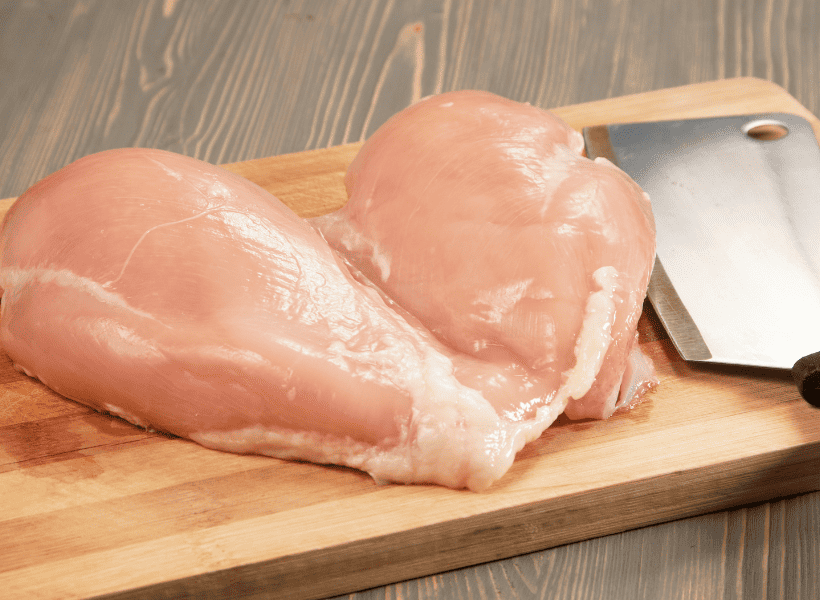 raw chicken breast on wooden cutting board with knife