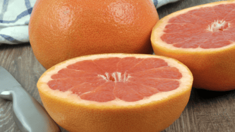 pink grapefruit cut in half beside whole grapefruit