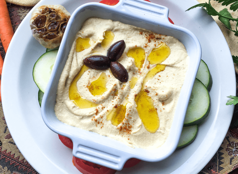 healthy homemade hummus in a serving dish with olives and olive oil