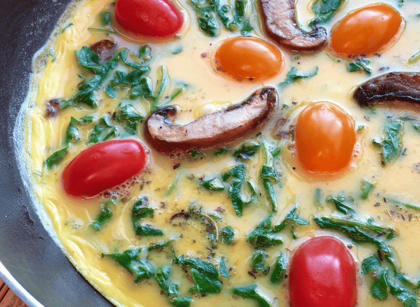 vegetable frittata cooking with arugula, tomatoes and mushrooms