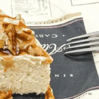 slice of cheesecake on a saucer with sliced apples and caramel on top