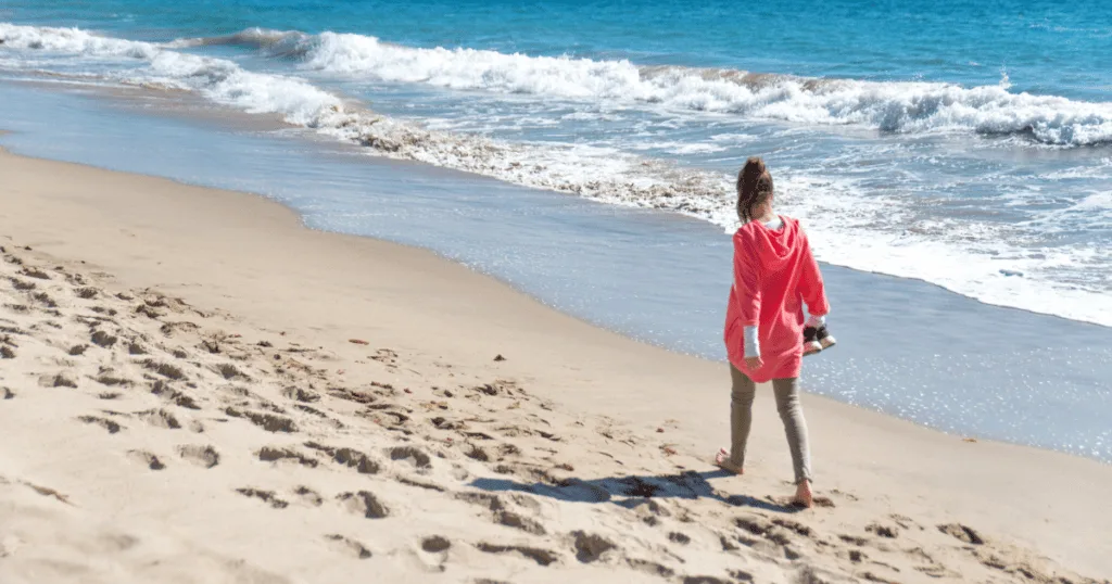 lady walking on beach holding shoes