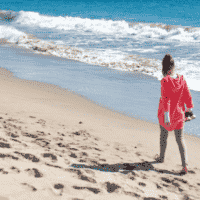 lady walking on beach holding shoes