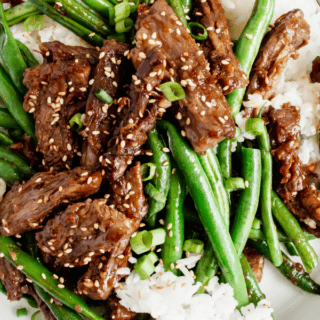 plate of stir fry beef and green beans with rice and sesame seeds