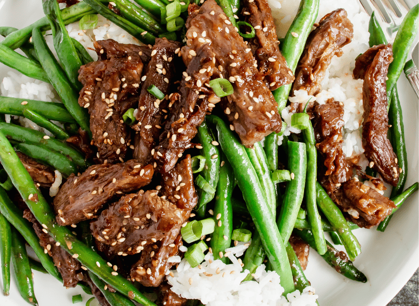 plate of stir fry beef and green beans with rice and sesame seeds