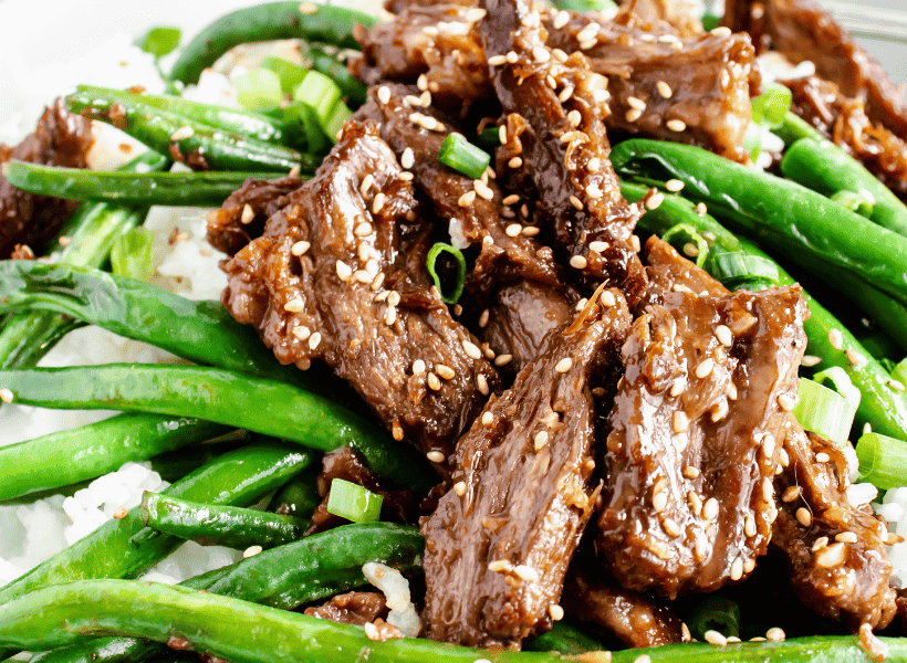 plate of beef and green beans with ginger sauce on bed of rice