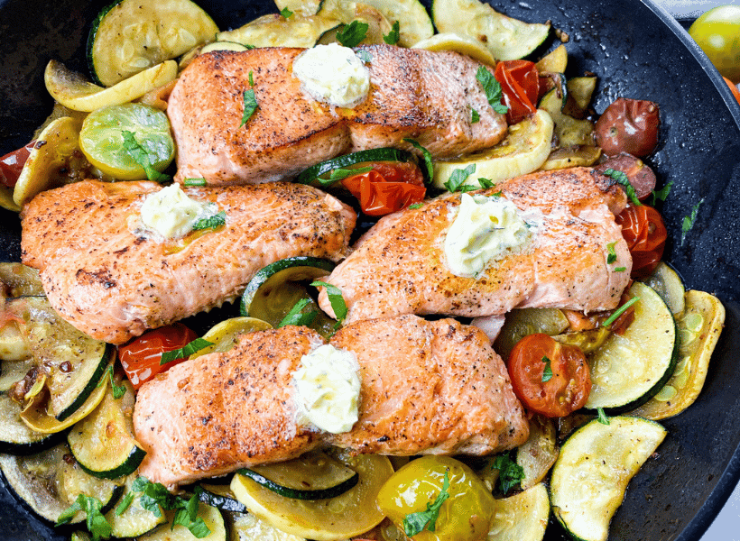 cast iron skillet with vegetables and perfectly cooked salmon with herb butter