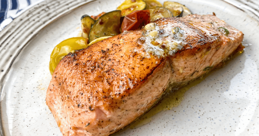 salmon with herb butter on a plate with vegetables