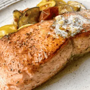 salmon with herb butter on a plate with vegetables