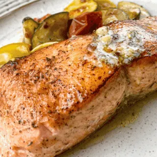 salmon with herb butter on a plate with vegetables