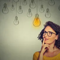 Thinking,Woman,In,Glasses,Looking,Up,With,Light,Idea,Bulb
