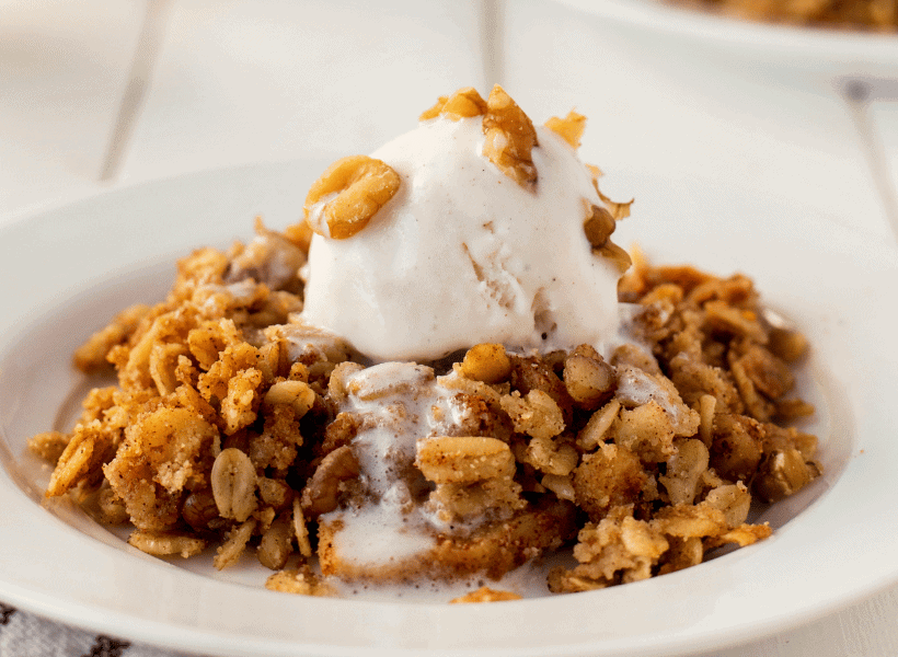 apple crisp in a white bowl with a scoop of vanilla ice cream on top