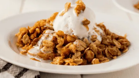 white bowl of apple crisp with vanilla ice cream on top