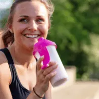 woman happy drinking a shake in a shaker cup outside sitting down