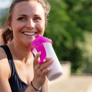woman happy drinking a shake in a shaker cup outside sitting down