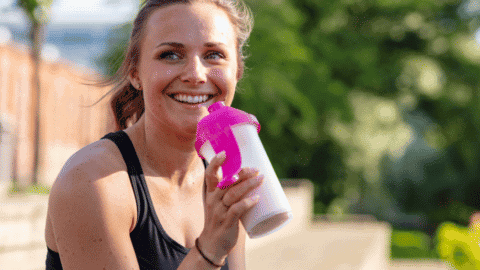 woman happy drinking a shake in a shaker cup outside sitting down