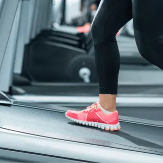 woman walking on incline treadmill with black leggings and pink walking shoes