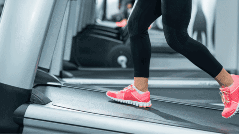 woman walking on incline treadmill with black leggings and pink walking shoes
