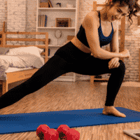 woman working out at home on a yoga mat with weights
