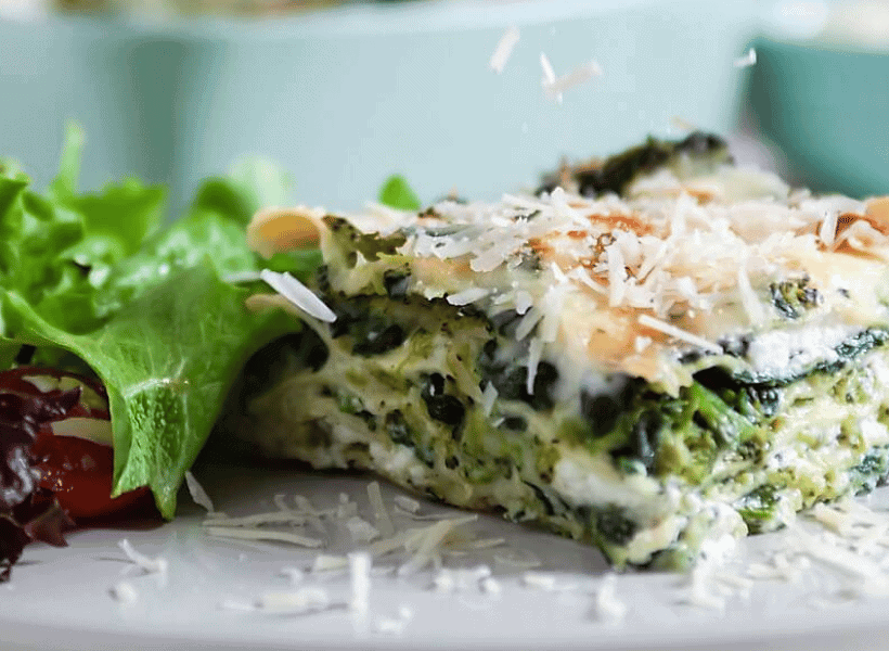 spinach and broccoli lasagna square on a white plate with salad