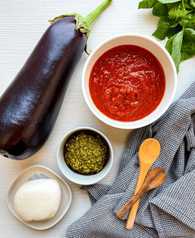 ingredients for eggplant parmesan without breadcrumbs marinara, pesto, mozzarella, eggplant and basil on counter